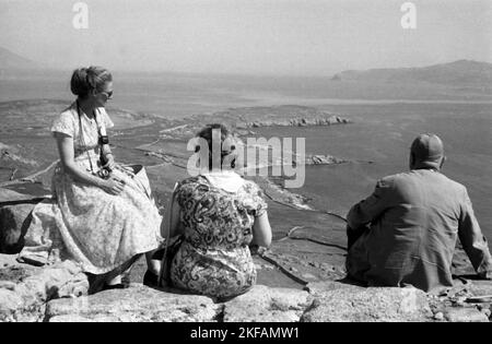 Griechenland - ein Mann und zwei Frauen sitzen auf einer Klippe auf der Insel Delos, Kykladen, und klicken auf die Bucht, 1954. Griechenland - Ein Mann und zwei Frauen sitzen auf einer Klippe auf der Insel Delos, Kykladen, werfen einen Blick in die Bucht, 1954. Stockfoto