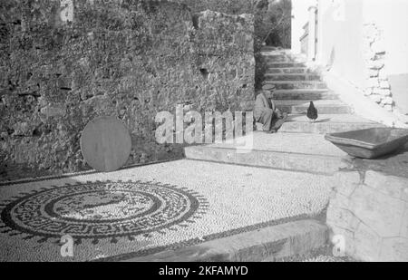 Ein Mann und ein Huhn in einer Gasse von Lindos auf Rhodos, Griechenland, 1950er Jahre. Ein Mann und eine Henne auf einer Gasse in Lindos auf der Insel Rhodos, Griechenland, 1950s. Stockfoto