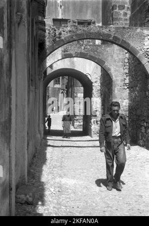 Ein Mann geht durch eine kleine enge Gasse in Griechenland, 1950er Jahre. Ein Mann, der in Griechenland durch eine schmale Gasse geht, 1950s. Stockfoto