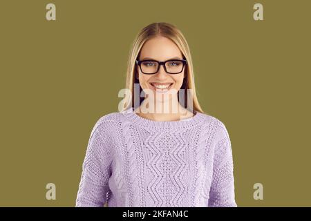 Junge lächelnde Frau in Brille und lila Pullover posiert auf khaki Hintergrund Blick auf die Kamera. Stockfoto