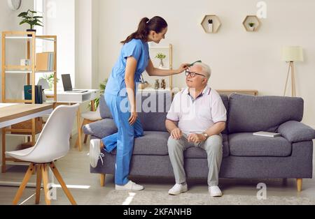 Freundliche junge Krankenschwester kämmt die Haare eines älteren Mannes, der im Pflegeheim auf dem Sofa sitzt. Stockfoto