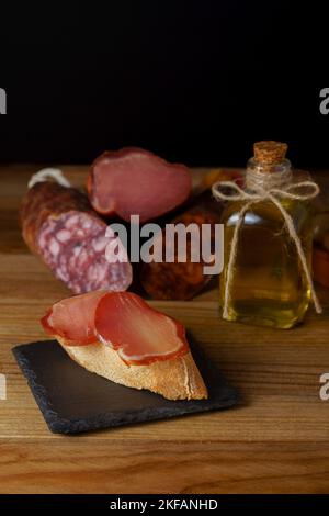 Tapa der iberischen Lende auf rustikalem Brot mit Olivenöl auf einem schwarzen Schiefer mit schwarzem Hintergrund Stockfoto