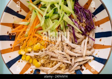 Draufsicht Schüssel mit kalten Nudeln mit geschreddertem Huhn und Gurke sowie Karotten- und Purpurkohl Stockfoto