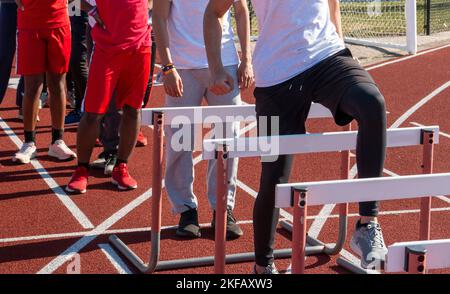 Ein High School blys Track Team, das während des Trainings über die Hürden der Rennstrecke läuft. Stockfoto