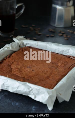 Hausgemachte leckere Schokoladenbrownies, frisch aus dem Ofen, der sich noch in der Backform befindet, bevor sie mit Kaffeekanne und Tasse in Quadrate geschnitten werden Stockfoto