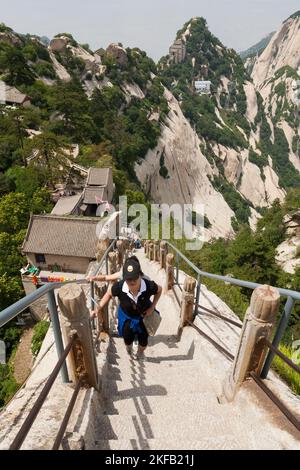 Besucher/Touristen steigen steile Stufen hinauf, die in einen Steinkamm geschnitten oder dort befestigt sind und zu einem der fünf Gipfel des Huashan-Berges/Berg Hua/Berg Hua in der Nähe von Huayin, Weinan, China, VR China führen. (125) Stockfoto