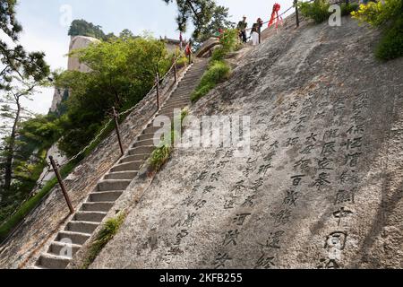 Besucher / Touristen steigen steile Stufen, die in eine Steinwand auf dem Huashan Berg / Mount Hua / Mt Hua in der Nähe von Huayin, Weinan, China, VR China, gehauen werden. (125) Stockfoto