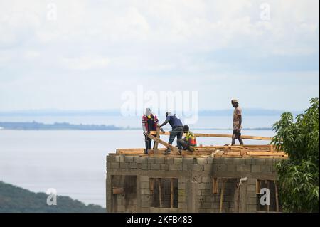 Bugala Island, Uganda - 30. Mai 2022: Bauarbeiter bauen ein Haus, stehen auf dem Dach, sonniger Tag im Mai Stockfoto