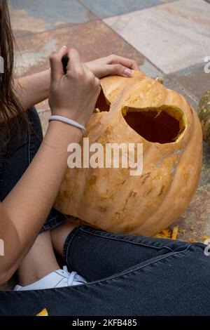 Junger Mann mit Bohrer oder dremel bohrt einen Kürbis für halloween Stockfoto