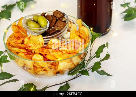 Bier vom Fass und Snacks auf weißem Hintergrund mit grünen Blättern. Sammlung von Snacks für Bier. Chips, Cracker und Oliven in transparenten Schalen. Stockfoto