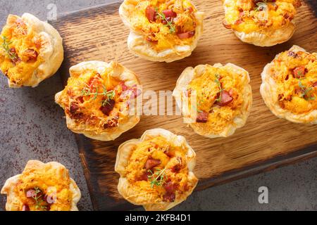 Hausgemachte Blättermuffins mit Schinken, Gemüse und Cheddar-Nahaufnahme auf einem Holzbrett auf dem Tisch. Horizontale Draufsicht von oben Stockfoto