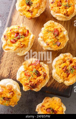 Rustikale Blätterteig-Muffins, gefüllt mit Eiern, Käse und Schinken aus nächster Nähe auf einem Holzbrett auf dem Tisch. Vertikale Draufsicht von oben Stockfoto