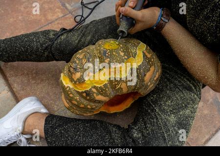 Junger Mann mit Bohrer oder dremel bohrt einen Kürbis für halloween Stockfoto