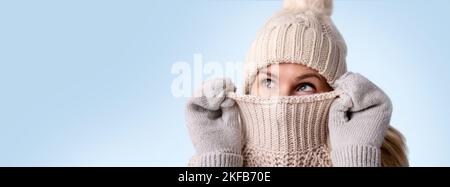 Frau in gestrickten Wollkleidung versteckt ihr Gesicht in Pullover und suchen isoliert auf blauem Hintergrund. Wintermode. Warme Kleidung. Banner mit Kopie s Stockfoto