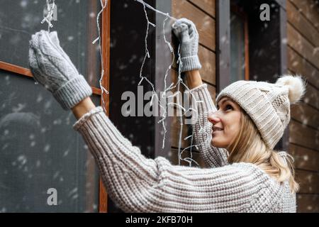 Weihnachtsdekorationen. Frau installieren elektrische weihnachtsschnur Lichter auf Haus Außenfassade Stockfoto
