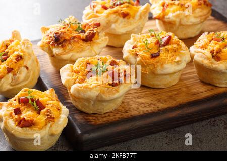 Hausgemachte Blättermuffins mit Schinken, Gemüse und Cheddar-Nahaufnahme auf einem Holzbrett auf dem Tisch. Horizontal Stockfoto