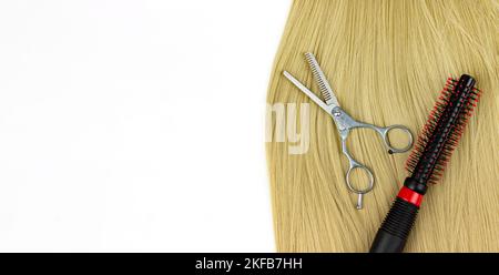 Professioneller Friseur rund Haarbürste und Schere mit Strang aus blondem Haar auf weißem Hintergrund. Serie: Professionelle Friseurausrüstung und Stockfoto