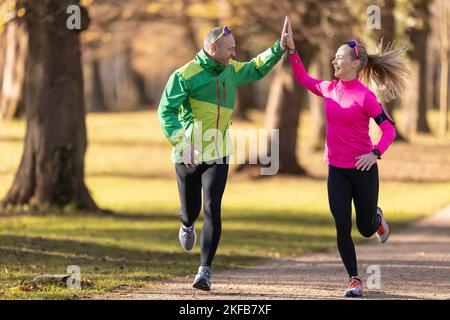 Zwei Läufer reifer Mann und junge Frau unterstützen sich gegenseitig und geben High-Five während eines Laufs. Stockfoto