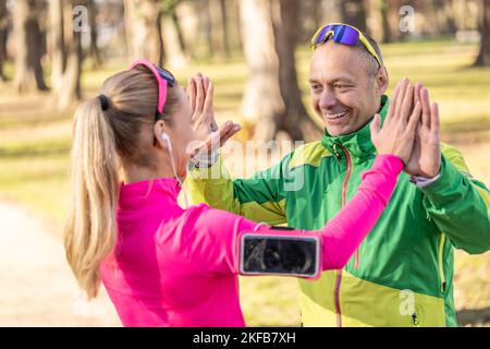 Ein reifer Mann und eine junge Frau unterstützen sich gegenseitig und geben High-Five nach einem Lauf. Stockfoto