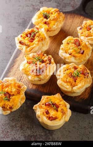 Herzhafte Blätterteig-Muffins mit Ei, Schinken und Cheddar-Käse aus nächster Nähe auf einem Holzbrett auf dem Tisch. Vertikal Stockfoto