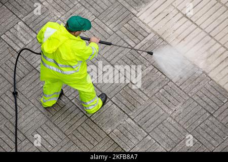 Arbeiter reinigen einen Gehweg mit Hochdruckwasserstrahl. Instandhaltung der öffentlichen Bereiche Stockfoto