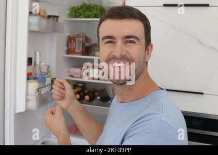 Lächelnder Mann mit offenem Kühlschrank im Hintergrund Stockfoto