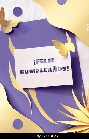 Feliz Cumpleanos Begrüßung auf Spanisch bedeutet Alles Gute zum Geburtstag. Frühling Geburtstag Gruß Papier Stil Kunst Design. Mehrlagiger, lila gelber Papierhintergrund Stockfoto