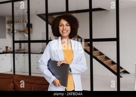 Selbstbewusste afrikanische Frau makler mit Laptop zeigt Wohnungen zum Mieten oder Kaufen. Hypothek für Wohnung für Kunden. Kreatives Foto für das Immobilienalter Stockfoto