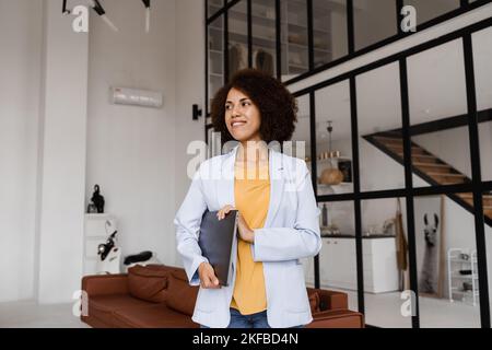 Selbstbewusste afrikanische Frau makler mit Laptop zeigt Wohnungen zum Mieten oder Kaufen. Hypothek für Wohnung für Kunden. Kreatives Foto für das Immobilienalter Stockfoto