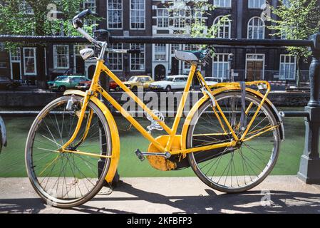 Amsterdam Fahrrad, Blick im Frühling auf ein altes gelbes Fahrrad, das neben einem Kanal im Zentrum der Stadt Amsterdam, Niederlande, Europa, geparkt ist Stockfoto