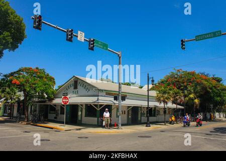 Famouse Green Parrot Bar mit Touristen an der Ecke und andere auf Motorroller mit heller Sonne und einem Royal Poinciana Baum in Blüte Key West Florida U Stockfoto