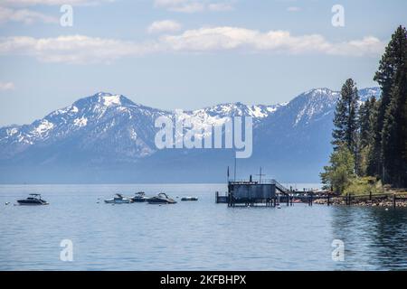 Lake Tahoe mit Booten und Dock mit amerikanischer Flagge im Vordergrund und schneebedeckten Bergen im Hintergrund - sehr blau Stockfoto