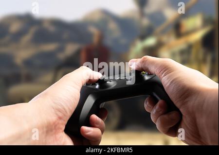 GAM22ICB Gamepad in den Händen eines Spielers vor dem Hintergrund eines spannenden Videospiels. Lustige Abenteuer Online-Spiele mit Freunden, Spaß Zeitvertreib, Modder Stockfoto