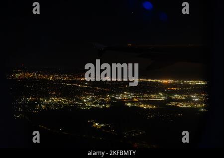 Fantastische Aussicht vom Flugzeugfenster. Blick auf die nächtliche Stadt, Metropole, beleuchtet von goldenen Lichtern. Schwarzer Nachthimmel. Wunderschöne Aussicht auf die nahe Stockfoto