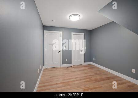 Innenansicht eines modernen Hauszimmers mit grauen Wänden, zwei weißen Türen und einer LED-Lampe Stockfoto
