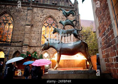 Bremen, Deutschland. 17.. November 2022. Die Bremer Stadtmusikanten stehen bei Regenwetter am Rathaus in der Innenstadt, während im Hintergrund bereits die Lichter des Weihnachtsmarktes leuchten. Der Weihnachtsmarkt auf dem Bremer Marktplatz beginnt am 21. November 2022. Quelle: Hauke-Christian Dittrich/dpa/Alamy Live News Stockfoto