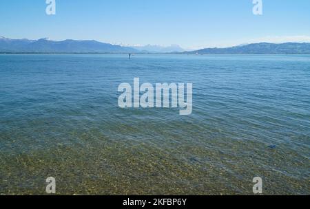 Wunderschönes blaues Wasser des Bodensees mit den Alpen im Hintergrund, von den Ufern der Insel Lindau an einem sonnigen Frühlingstag gesehen, Deutschland Stockfoto