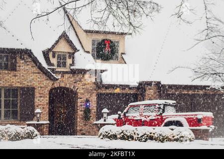 Rotes Pickup-Utility-Vehicle vor dem Haus geparkt, das zu Weihnachten im Schnee mit Laternen und Kranz geschmückt ist Stockfoto
