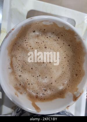 Geschlagene Kaffeetasse auf dem Tisch, flauschige Kaffeetasse im Tablett, schaumiger Kaffee Stockfoto