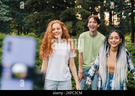 Drei Jugendliche Schöpfer tanzen, während Online-Videos mit Telefon im Park streamen. Social-Media-Challenge-Netzwerk-App. Video-Streaming. Mobiltelefon Stockfoto
