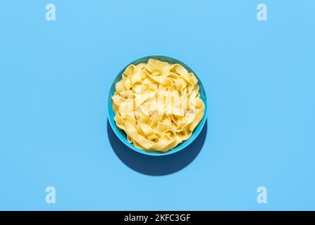 Draufsicht mit einer Schale mit gekochter Pappardelle, minimalistisch auf einem blauen Tisch. Einfache, einfache Nudeln in hellem Licht auf einem lebhaften, farbigen Hintergrund Stockfoto