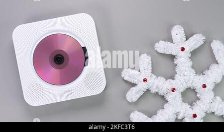 Eleganter, tragbarer, weißer CD-Player mit pinkfarbener cd, auf der Weihnachtsmusik mit weißer Schneeflocke auf grauem Hintergrund abgespielt wird. Trend im Retro-Vintage-Stil Stockfoto