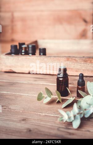 Ätherische Öle in kleinen Glasflaschen mit Eukalyptus-Zweige auf Holzhintergrund. Selektiver Fokus- und Kopierbereich für Text. Naturkosmetikprodukte. Stockfoto