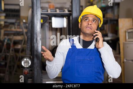 Lateinamerikanischer Mann in blauen Overalls telefoniert im Baumarkt Stockfoto