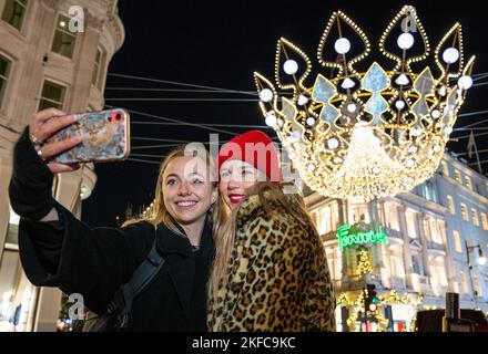 NUR FÜR REDAKTIONELLE VERWENDUNG Alethea Norman-Rhods und Anna Beketov machen ein Selfie vor dem Lichtdesign zu Ehren von Queen Elizabeth II., das im Rahmen der jährlichen Weihnachts-Lichtschalter-Veranstaltung in der Bond Street in London enthüllt wird. Bilddatum: Donnerstag, 17. November 2022. Stockfoto