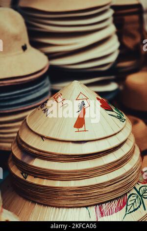 Eine vertikale Aufnahme von Stapel von vietnamesischen konischen Hüten mit asiatischen Symbolen Stockfoto