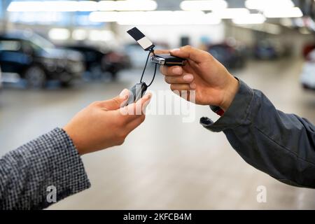 Der Automechaniker gibt die Schlüssel den Kunden, die den Kaufvertrag unterzeichnet haben Stockfoto