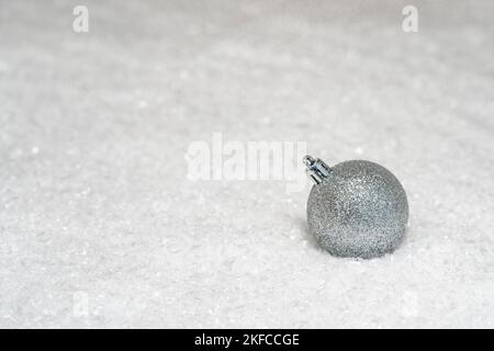 Silberner Glitzerkugel, weihnachtsbaumschmuck, auf dem Schnee Stockfoto