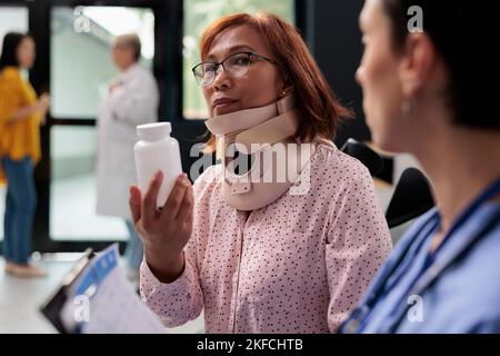 Traumatologin Krankenschwester, die verletzten Patienten Flaschentabletten gibt und ihnen die medikamentöse Behandlung erklärt, um bei Krankheitsschmerzen zu helfen. Ältere Frau mit Halsband, die sich in der Krankenhauslobby beraten hat Stockfoto