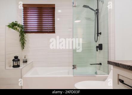 Badewanne mit Glasduschpaneelen und Toilette im Badezimmer in einem modernen Haus. Stockfoto